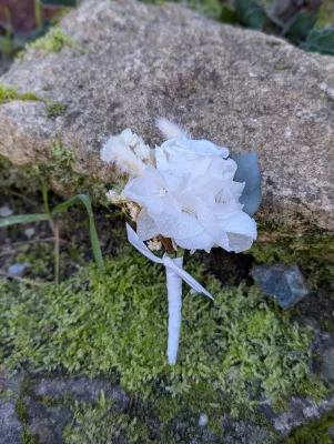 Boutonnière de mariage bohème élégante avec une rose blanche, de l'eucalyptus et des fleurs séchées, pour le marié.