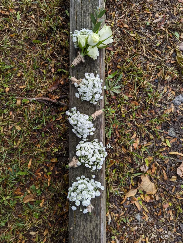 Boutonnière champêtre et élégante avec une rose blanche, de l'eucalyptus et du gypsophile pour un mariage d'été.