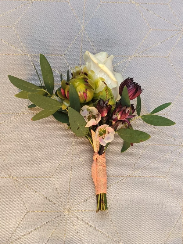 Boutonniere delicate pour mariage champetre, composee d'une rose blanche, petites fleurs pourpres et feuillage eucalyptus.