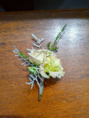 Boutonnière de mariage classique en rose crème, eustoma vert pâle et feuillage argenté, élégante pour un mariage.