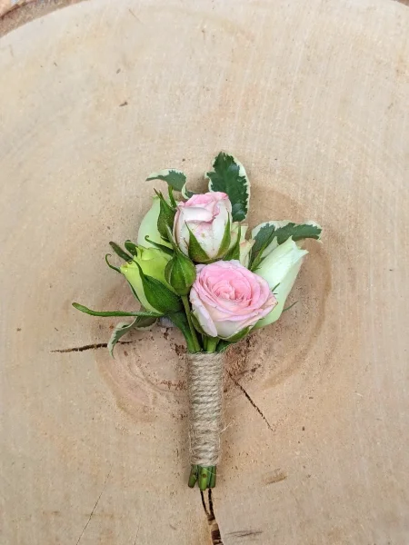 Boutonnière champêtre pour homme avec deux roses poudrées et feuillage panaché, ficelée de jute.