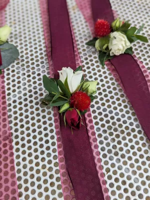 Collection de boutonnières champêtres pour mariage, comprenant des roses blanches et rouges, une fleur rouge pompon, eucalyptus et feuillage.