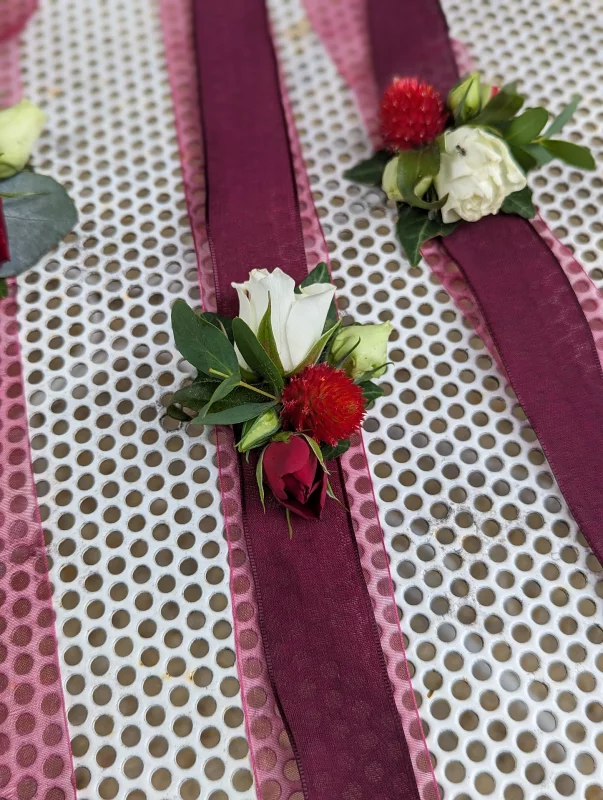 Rustic Wedding Buttonhole Collection, featuring white and red roses, a red pompom flower, eucalyptus and foliage.