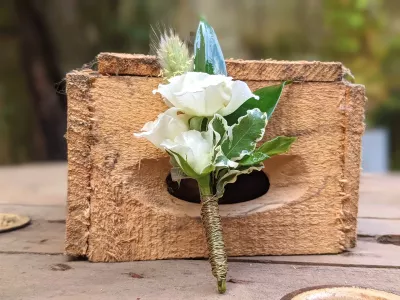 Boutonnière de mariage champêtre avec roses blanches, feuillage panaché et graminées, élégamment ficelée, sobre.