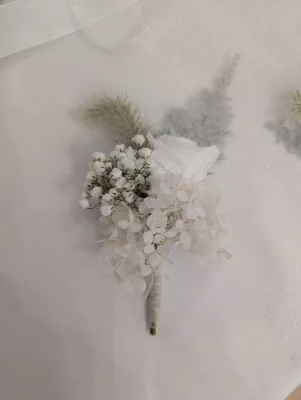 Sophisticated country-style buttonhole with white rose, gypsophila, and foliage for a wedding.