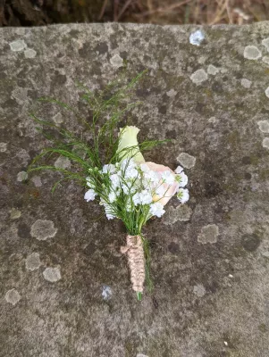Boutonnière champêtre avec bouton de rose crème, gypsophile et feuillage fin, attachée avec de la ficelle de jute.