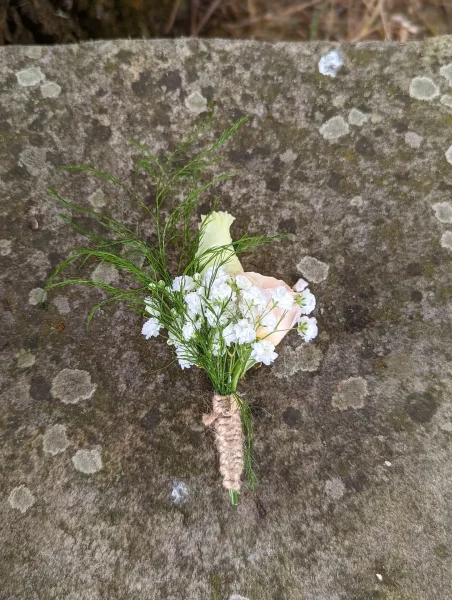 Boutonnière champêtre avec bouton de rose crème, gypsophile et feuillage fin, attachée avec de la ficelle de jute.