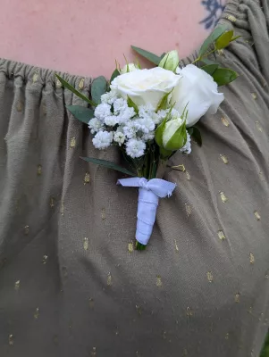Boutonnière délicate style champêtre avec roses blanches, gypsophile et feuillage vert pour mariage.