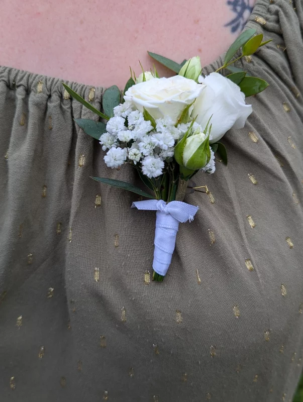 Delicate country-style buttonhole featuring white roses, gypsophila and green foliage for a wedding.