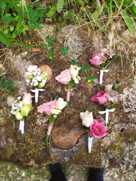 Collection de boutonnières de mariage champêtre avec roses, gypsophile et feuillage, certaines attachées avec du ruban blanc.