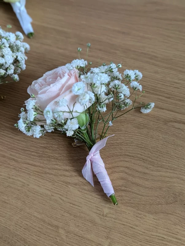 Boutonnière de mariage classique avec une rose rose pâle et du gypsophile, idéale pour le marié ou les témoins.