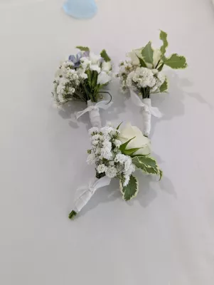 Boutonnière classique délicate avec rose blanche, gypsophile et feuillage panaché pour mariage.