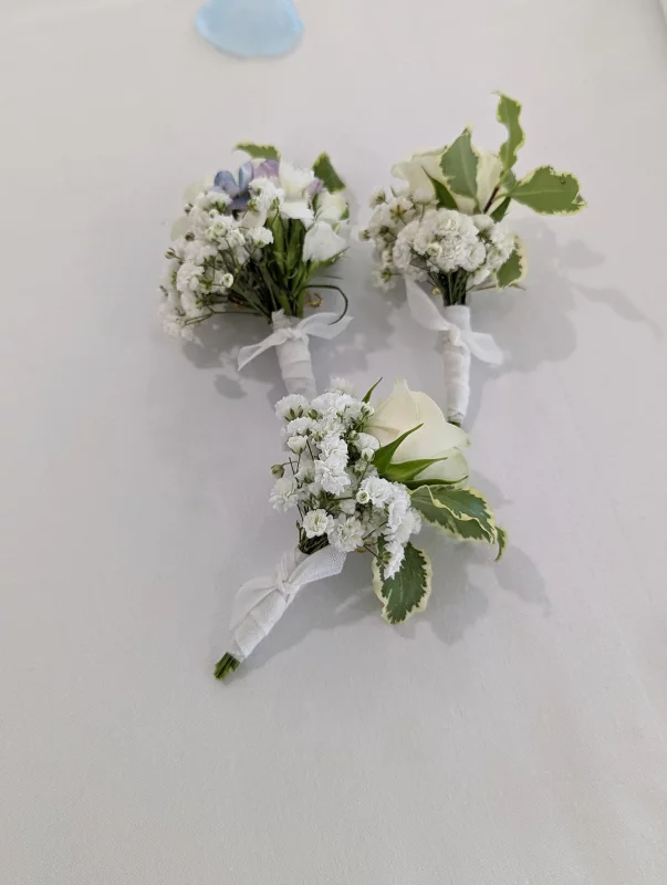A delicate classic buttonhole featuring a white rose, gypsophila and variegated foliage for a wedding.