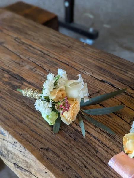 Boutonnière de mariage classique, avec des roses jaune pâle, des petites fleurs blanches et des feuilles d'olivier.