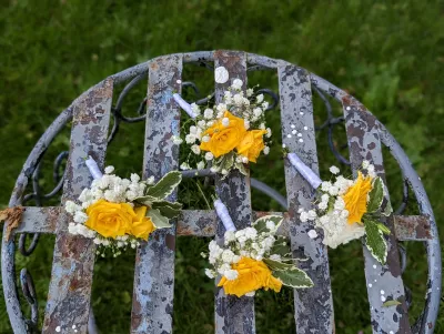 Boutonnières champêtres élégantes avec roses jaunes, gypsophile et feuillage panaché, complétant le thème du mariage.