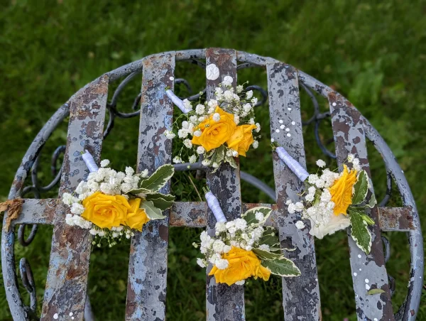 Boutonnières champêtres élégantes avec roses jaunes, gypsophile et feuillage panaché, complétant le thème du mariage.