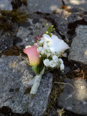 Boutonnière romantique organique avec rose rose, lisianthus blanc et gypsophile sur pierre.