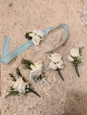 Boutonnières et bracelet floral classiques avec roses blanches, lisianthus et verdure givrée pour mariage d'hiver.