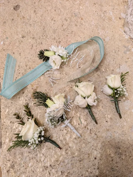 Boutonnières et bracelet floral classiques avec roses blanches, lisianthus et verdure givrée pour mariage d'hiver.