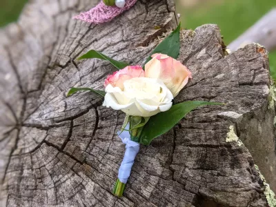 Boutonnière classique avec rose blanche, rose crème et feuillage vert pour costume de mariage.