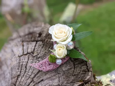 Boutonnière classique avec roses blanches, feuillage vert, maillage rose et perles nacrées pour mariage.