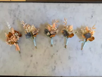 Cinq boutonnières bohèmes en fleurs séchées, avec chardons, hortensias et herbes, parfaites pour un mariage rustique.