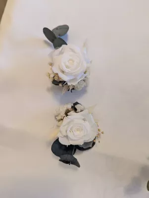 Deux élégantes boutonnières de mariage assorties, featuring roses crème éternelles, eucalyptus et accents de fleurs séchées.