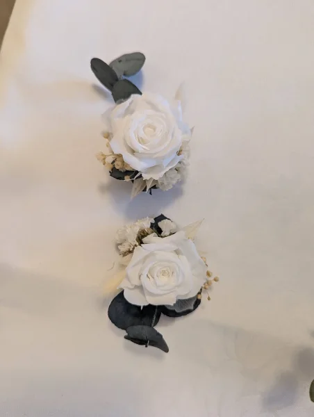 Deux élégantes boutonnières de mariage assorties, featuring roses crème éternelles, eucalyptus et accents de fleurs séchées.