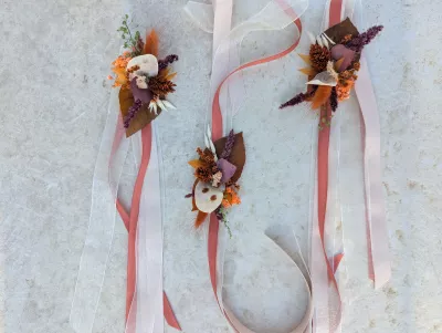 Floral bracelets with dried orange, terracotta and burgundy flowers, adorned with ribbons for a wedding.