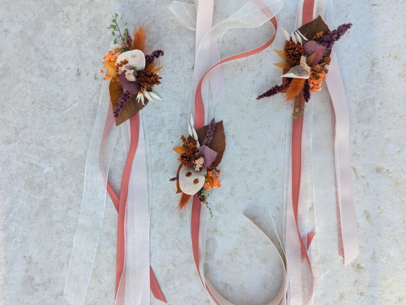 Floral bracelets with dried orange, terracotta and burgundy flowers, adorned with ribbons for a wedding.