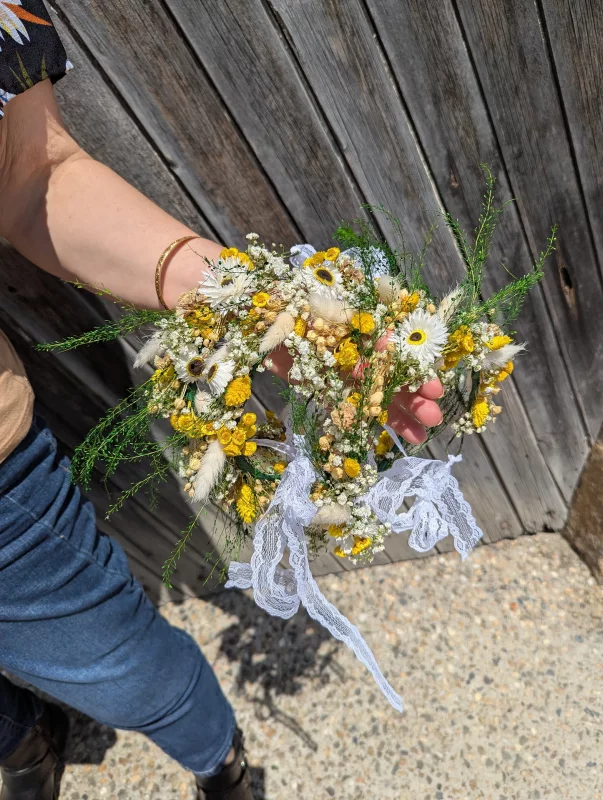 Bohemian-country style bridal floral bracelet, featuring delicate white daisies, vibrant yellow craspedia, and airy gypsophila, nestled amongst verdant green foliage.