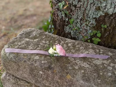 Bracelet floral champêtre avec petite rose rose, fleurs blanches et feuillage, fixé sur un ruban quadrillé rose pâle.