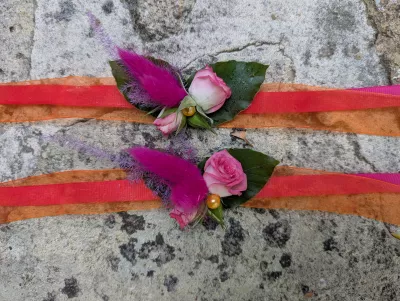 Sophisticated country-style floral bracelets with pale roses, foliage and fuchsia feathers for a wedding.