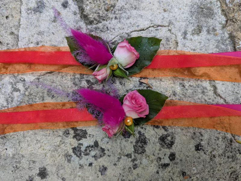 Sophisticated country-style floral bracelets with pale roses, foliage and fuchsia feathers for a wedding.