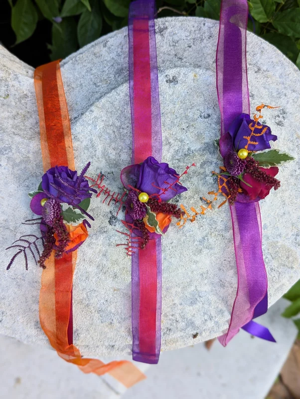 Bracelets floraux avec roses violettes et orange, rubans assortis pour mariage.