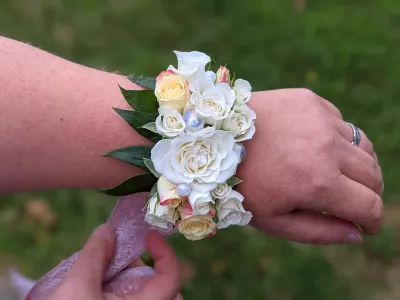 Bracelet floral classique avec roses blanches, crèmes et jaunes pâles, feuillage vert et perles décoratives pour mariage à Arsac.