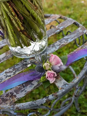Bracelet floral champêtre pour mariage, composé de mini roses, chardon bleu et feuillage, agrémenté d'un ruban violet.