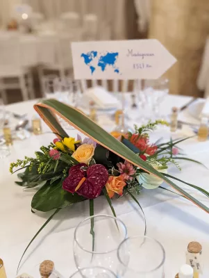 Centre de table exotique avec anthuriums rouges, roses et orchidées, orné de feuillage tropical pour un mariage d'été.
