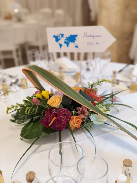 Centre de table exotique avec anthuriums rouges, roses et orchidées, orné de feuillage tropical pour un mariage d'été.