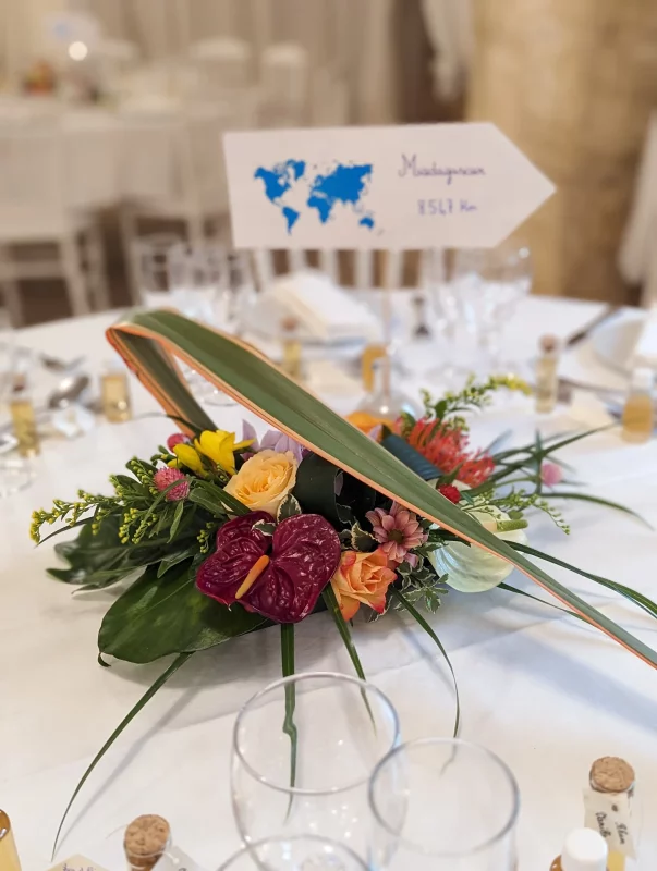 Exotic table centrepiece with red anthuriums, roses and orchids, adorned with tropical foliage for a summer wedding.