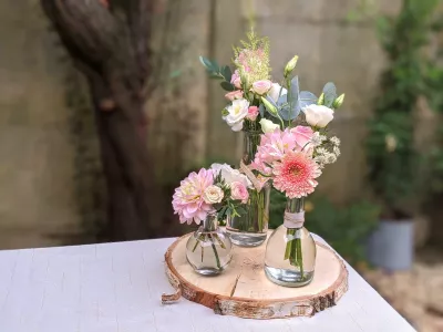 Centre de table champêtre pour mariage avec dahlias rose poudré, roses crème et feuillage vert frais, sur un rondin de bois.