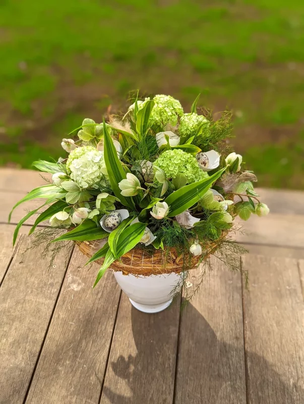 Centre de table champêtre pour mariage printanier, avec hortensias vert clair, hellébores crème et feuillages délicats.