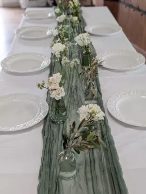 Centre de table champêtre pour mariage, avec des œillets blancs, roses pâles, branches d'olivier dans de petits vases en verre, ambiance naturelle.