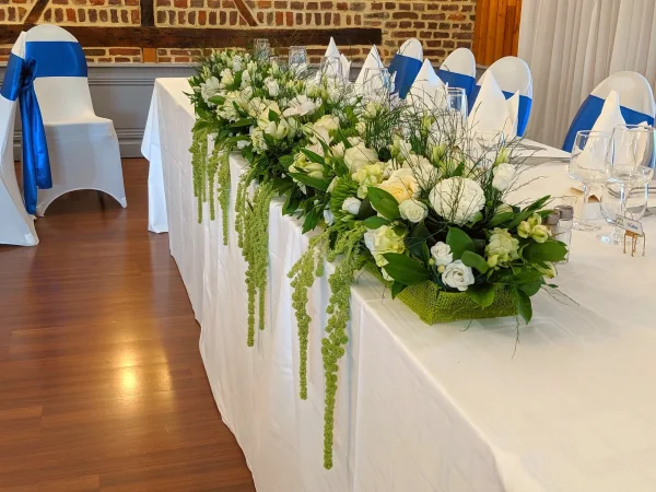 Centre de table élégant et classique pour mariage, avec des orchidées blanches, des roses et un feuillage vert printanier retombant.