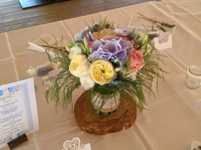Centre de table champêtre avec roses jaunes et roses, hortensias bleus et feuillage luxuriant, pour un mariage estival.