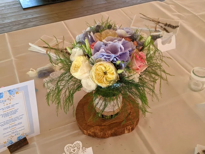 Centre de table champêtre avec roses jaunes et roses, hortensias bleus et feuillage luxuriant, pour un mariage estival.