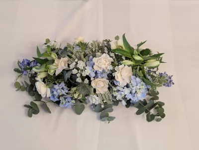 Composition florale de centre de table allongée classique avec roses, hortensias bleus, lys et eucalyptus pour mariage.