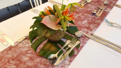 Centre de table exotique pour un mariage, avec anthurium rose, gloriosa orange, feuillage monstera et ananas. Création florale audacieuse.