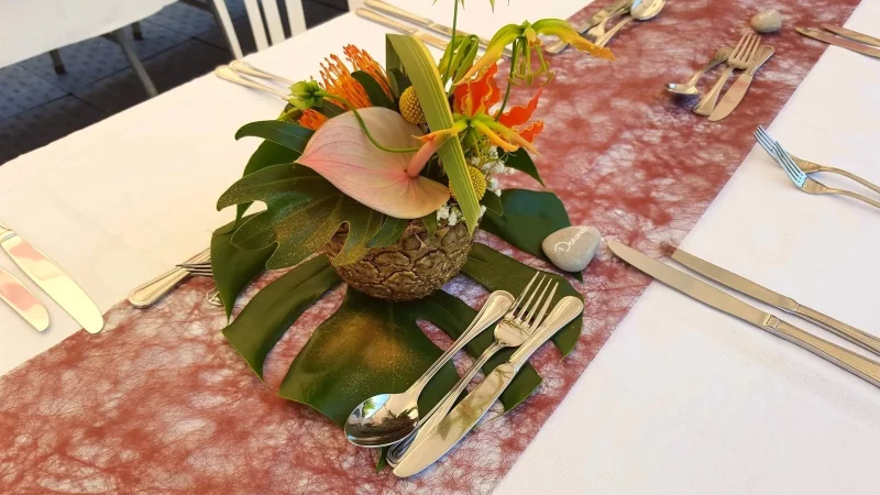 Centre de table exotique pour un mariage, avec anthurium rose, gloriosa orange, feuillage monstera et ananas. Création florale audacieuse.