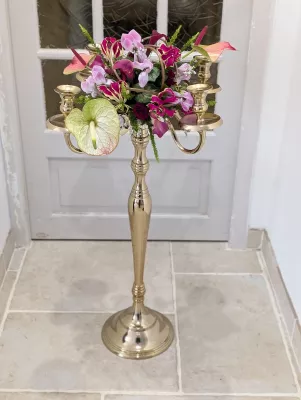 Centre de table de mariage exotique et classique avec anthuriums, orchidées roses et feuillage vert sur un candelabre doré.